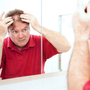 An image of a man inspecting his hair loss to promote the homeopathic patches for hair restoration from Frequency Apps.