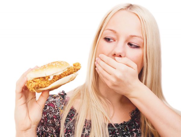 Woman holding a chicken sandwich and covering her mouth, representing the benefits of the Appetite Suppressant Patch